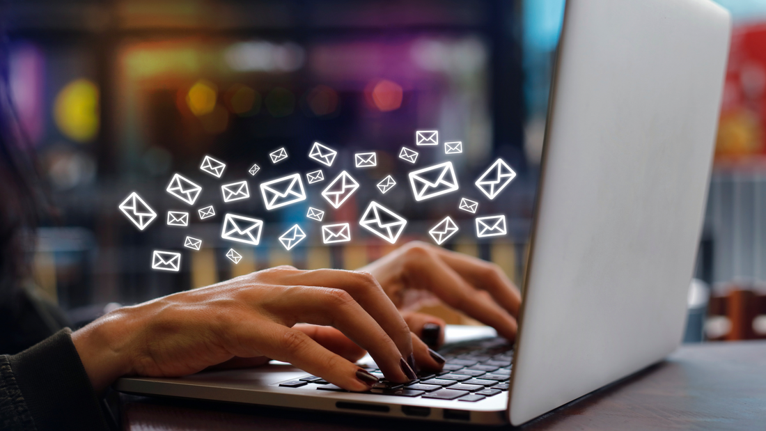 picture of a person's hands typing on a laptop, screen not shown. with little email letter emojis flying over the hands. 